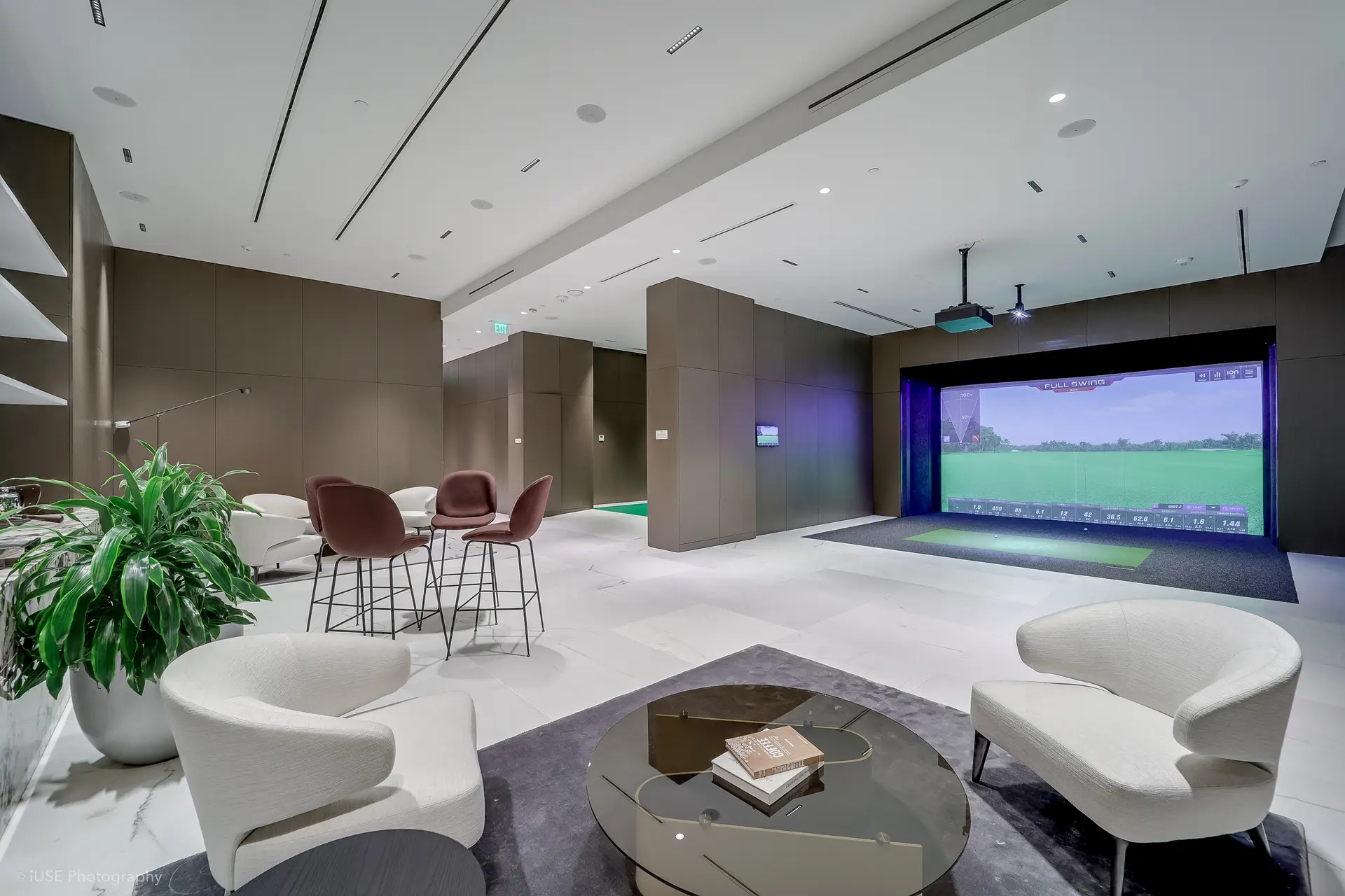 Golf simulator room at Aston Martin Residences featuring modern chairs and a green screen setup.