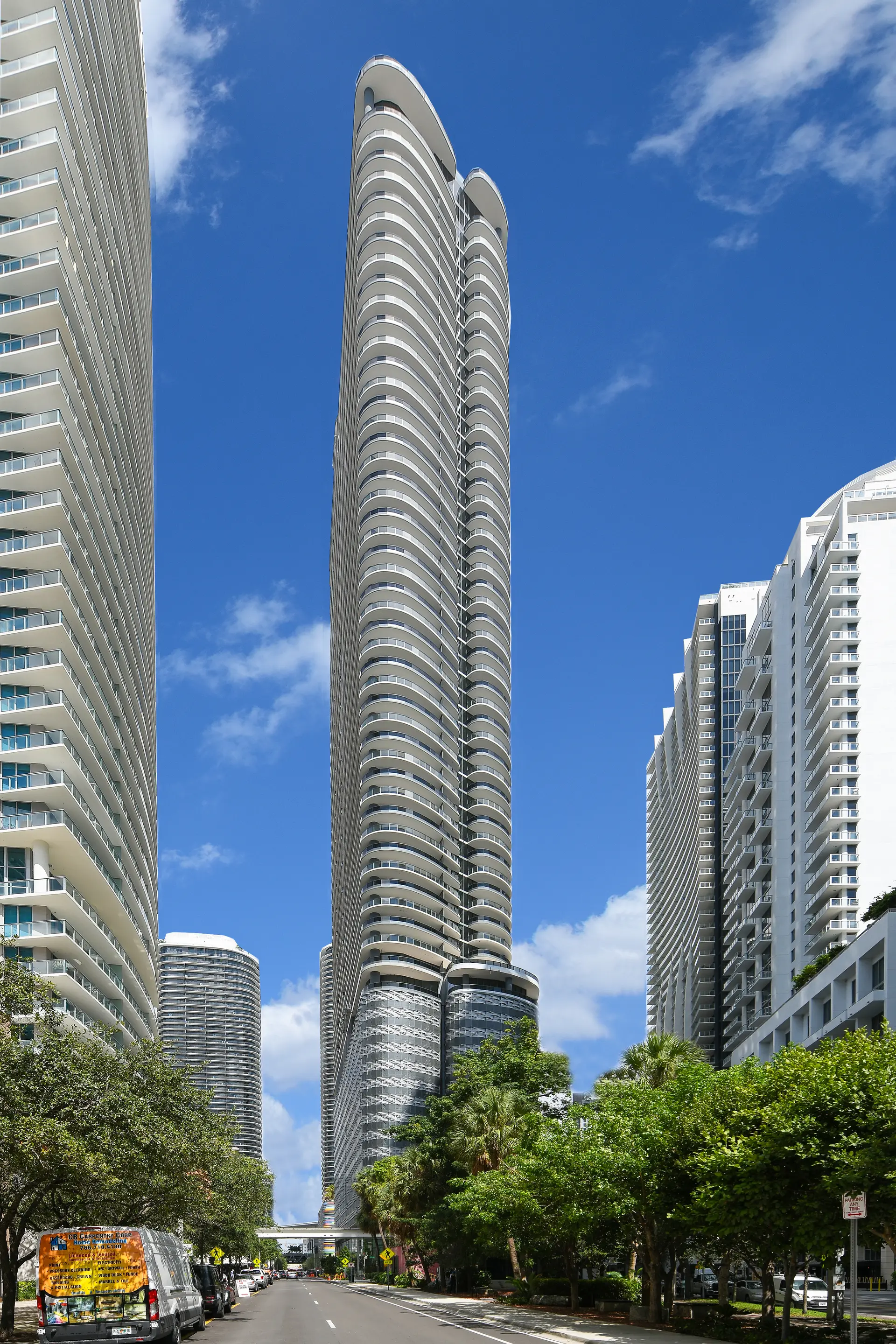 Brickell Flatiron tower in Miami viewed from the street, surrounded by trees.