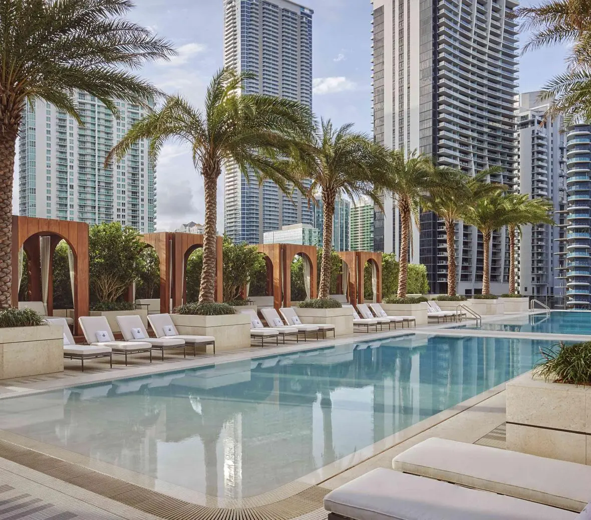 SLS Lux pool deck with palm trees and high-rise views in Miami.